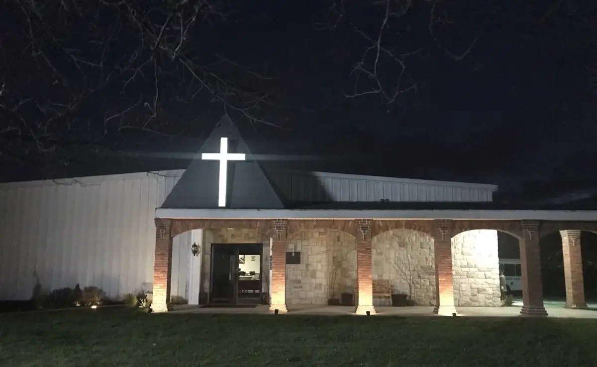 Monticello Gospel Assembly at night, a lit cross above the stone arches